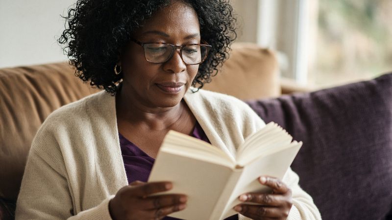 A woman in reading glasses absorbed in a book on the sofa